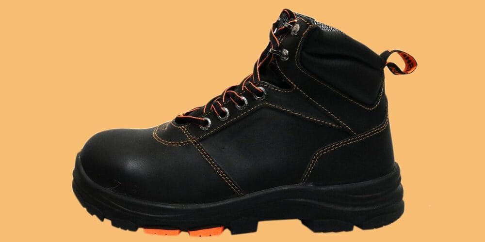 Black safety work boot with orange stitching and laces on an orange background with a little heel.