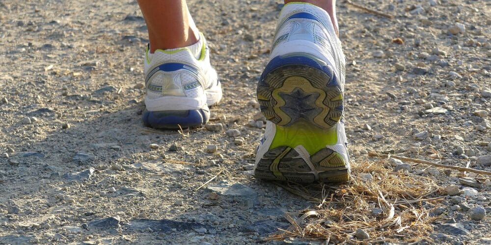 Close-up of a person walking on a rocky path wearing white and blue best soles running shoes