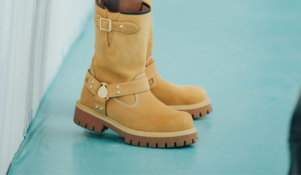 Tan leather boots with buckled straps and rugged soles are placed on a light blue floor.