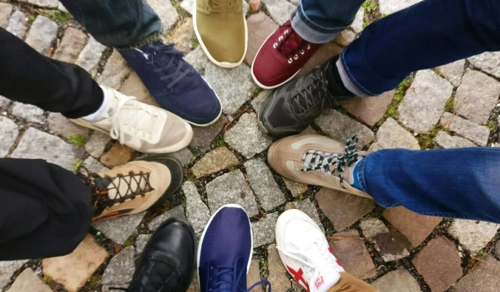 Top view of a group of people wearing different walking shoes standing in a circle on cobblestone pavement.