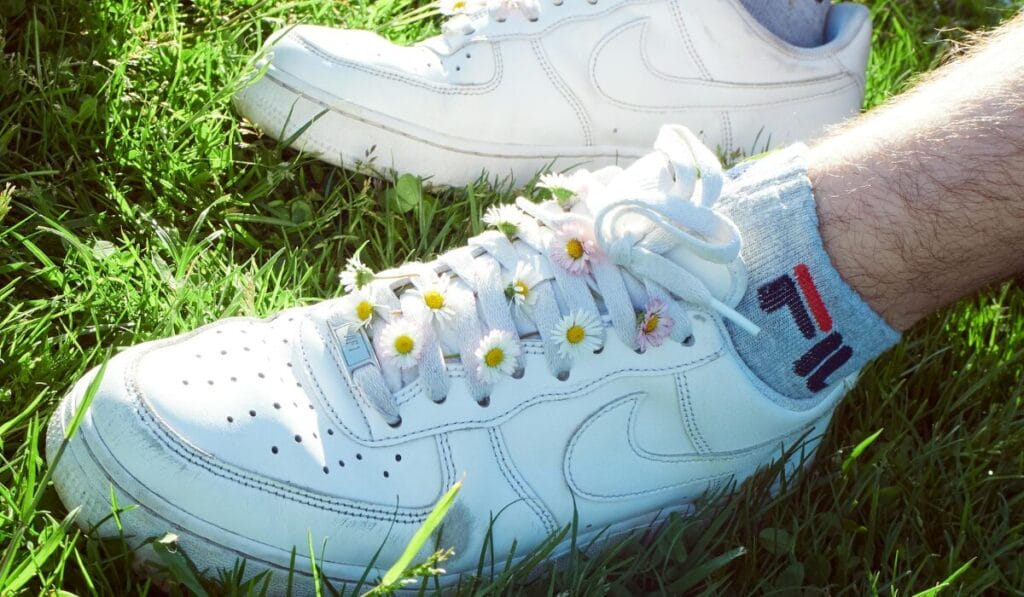 White walking shoes on green grass with small flowers tucked into the laces – stylish and casual outdoor look.