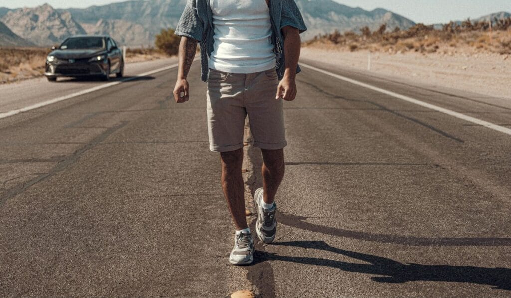 A Man walking on a dry road wearing athletic sneakers in a desert area