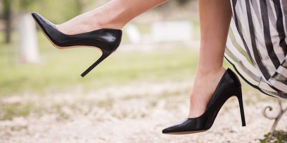 A woman wearing black high-heeled shoes without socks, outdoors, with a striped dress