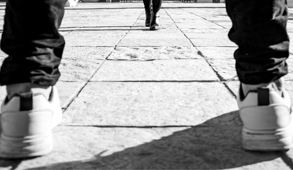 Close-up of two people walking on a paved path, showing only their shoes and legs – highlighting walking motion and footwear.