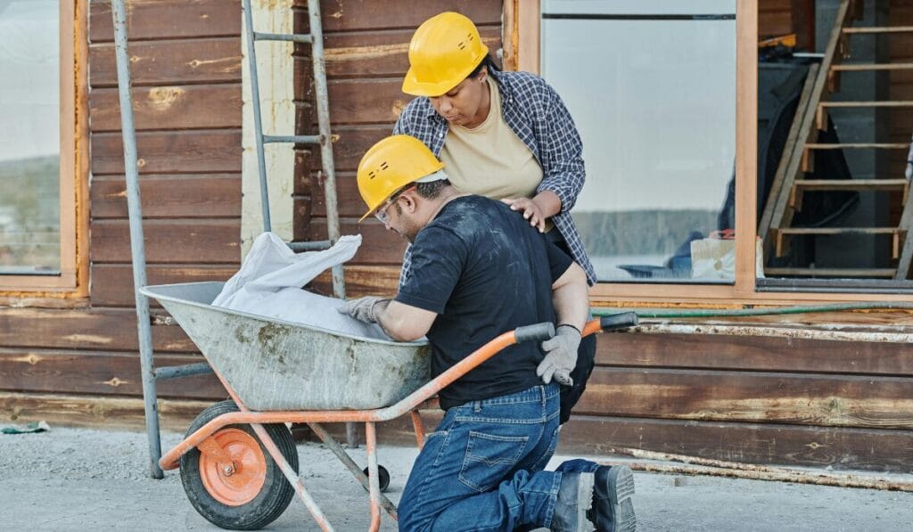 Construction workers discussing blueprints while kneeling, wearing safety helmets at a building site.