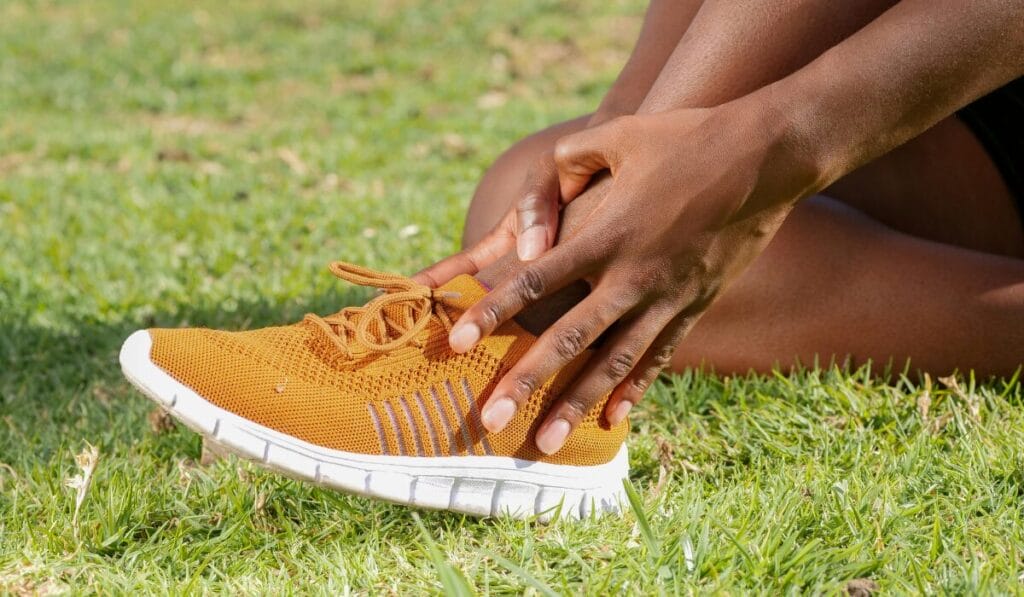 Man tying orange walking shoe laces while sitting on grass - knee support footwear for outdoor activity.