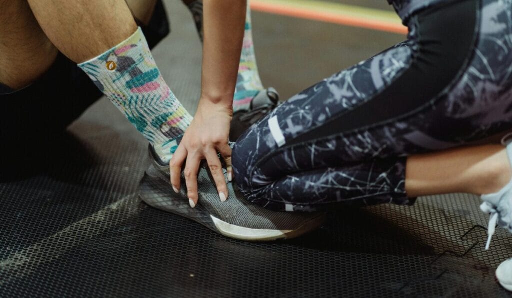 Trainer supporting athlete’s foot with black walking shoes on gym mat - helping with knee pain support.