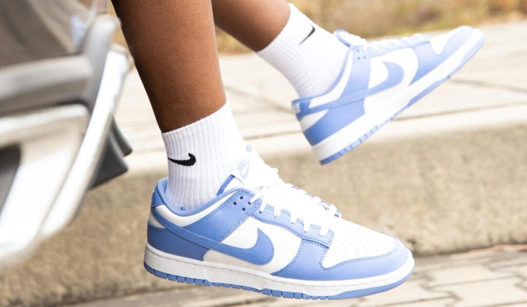 A Person stepping out of a car wearing white and light blue Nike sneakers with white Nike socks.