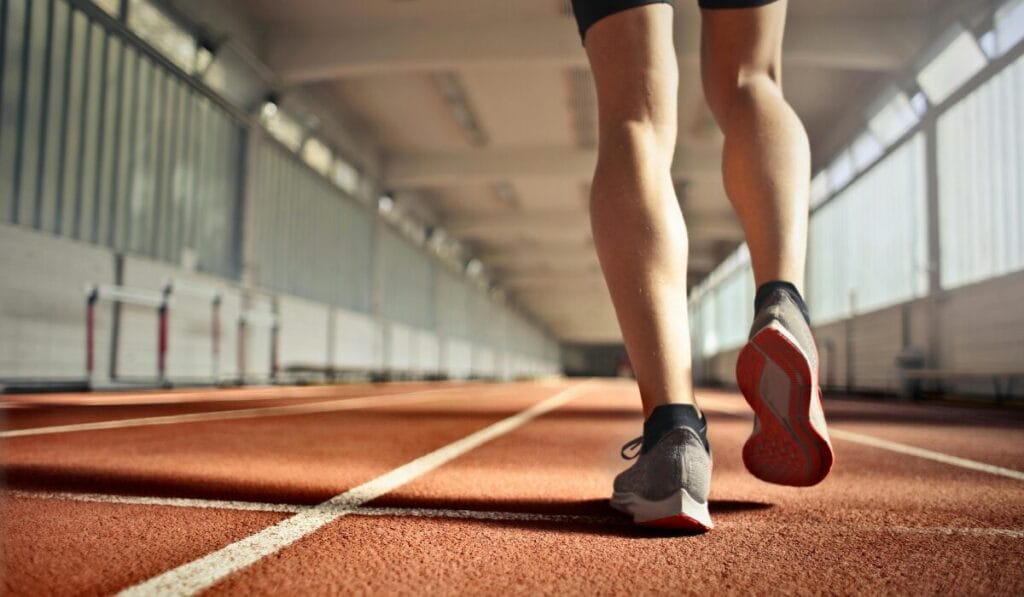 A person running on an indoor track, focusing on shoes and legs