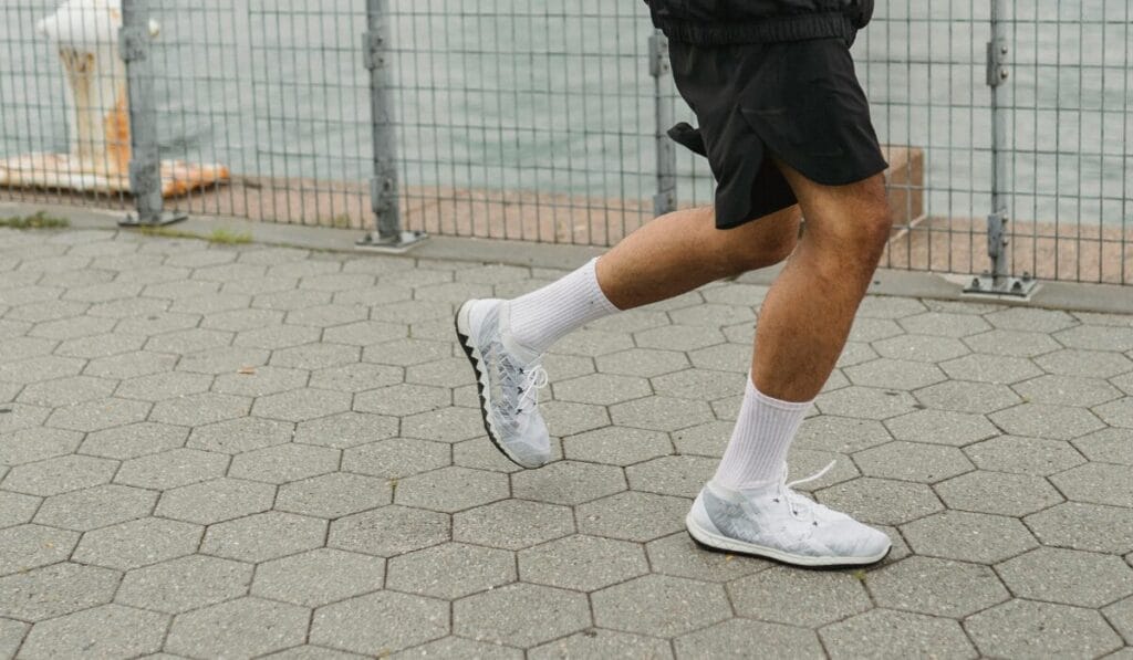 Man wearing white athletic running shoes while jogging on a paved pathway outdoors