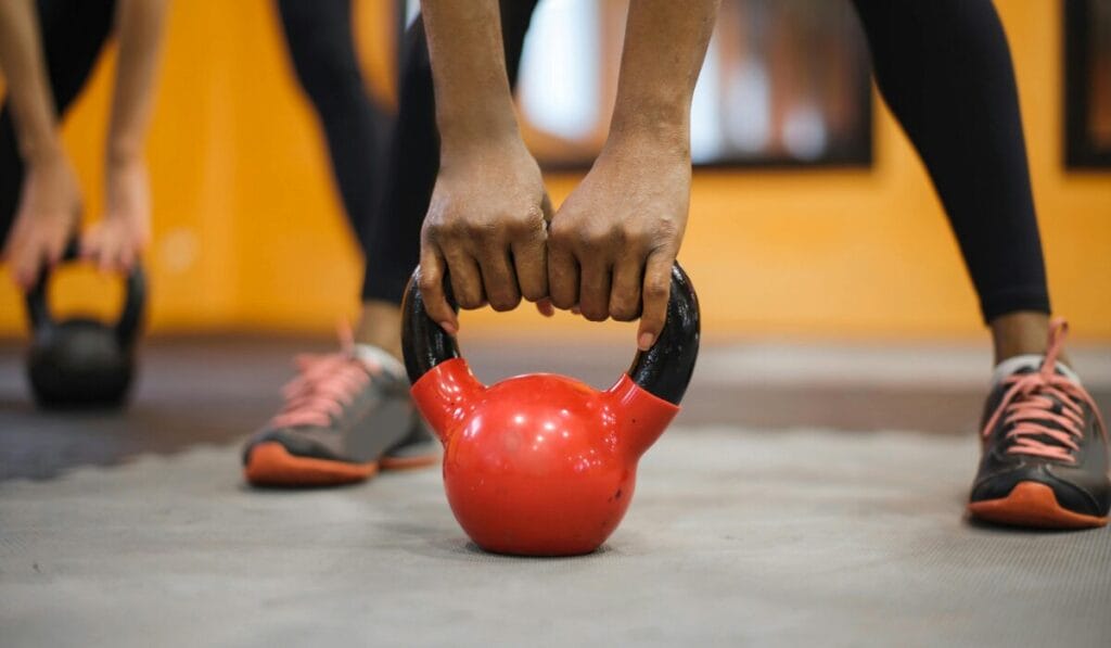 Close-up of a person wearing sports shoes lifting a red kettlebell in a gym