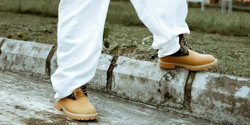 A Person wearing tan leather walking boots stepping on a concrete curb outdoors